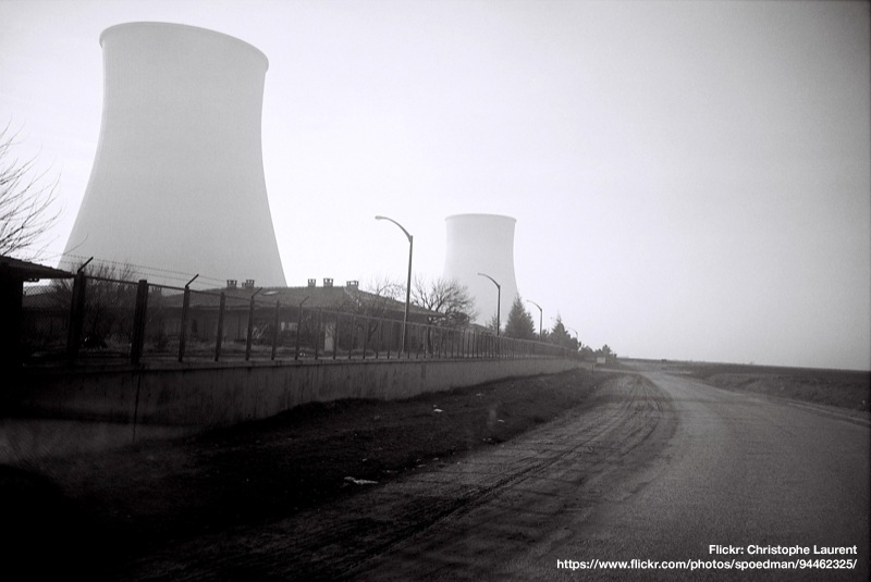 black and white of two nuclear cooling towers in the distance shrouded in fog with a gravel road winding in the foreground