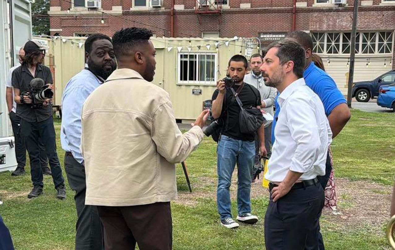 Former Transportation Secretary Pete Buttigieg standing with four others in a circle while having a conversation in Little Rock, Arkansas.